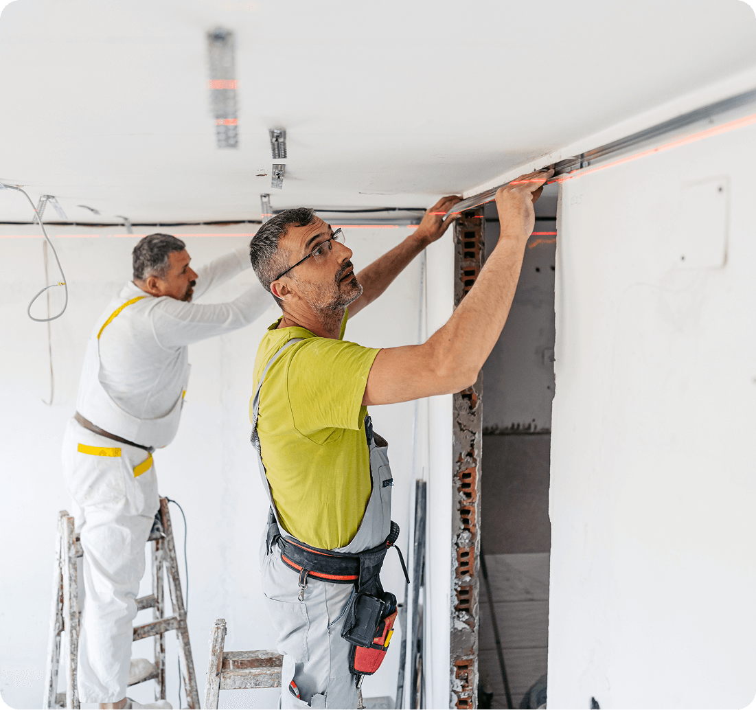 Two workers installing ceiling fixtures indoors.